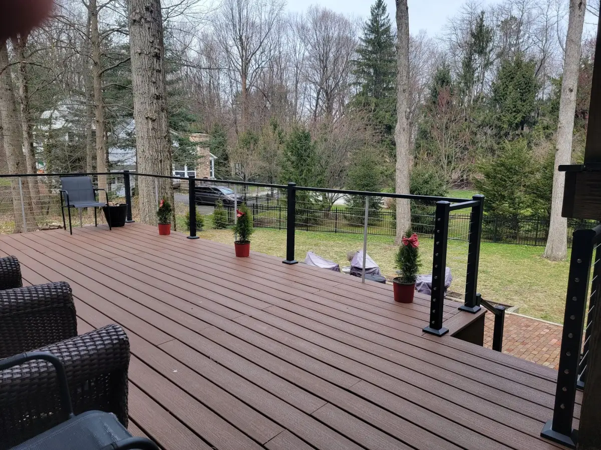 Composite deck with black aluminum posts and stainless cable railing overlooking a wooded backyard